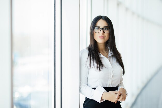 Geschäftsfrau in Gläsern kreuzte Hände Porträt im Büro mit Panoramafenstern. Geschäftskonzept