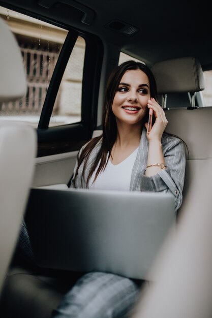 Geschäftsfrau in ihrem Auto mit einem Laptop und einem Mobiltelefon