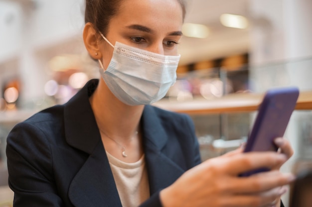 Geschäftsfrau mit der medizinischen Maske, die ihr Telefon betrachtet