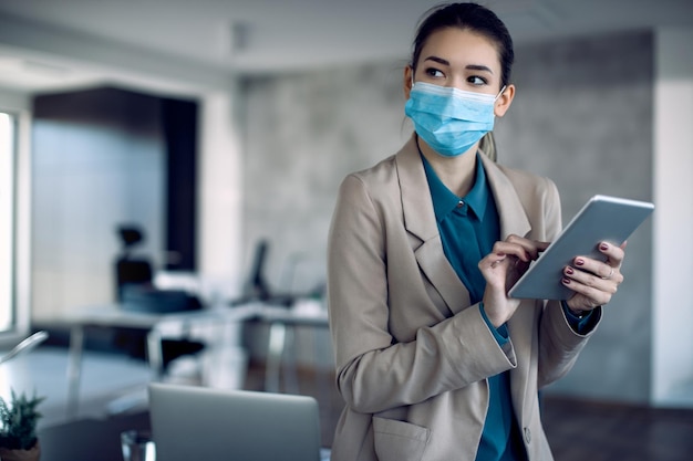 Geschäftsfrau mit Gesichtsmaske mit digitalem Tisch während der Arbeit im Büro