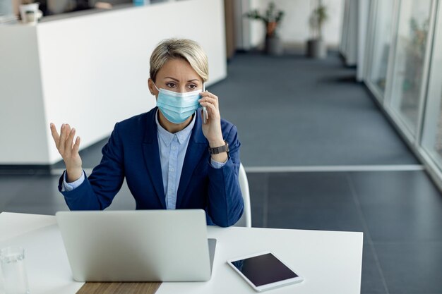 Geschäftsfrau telefoniert, während sie im Büro eine schützende Gesichtsmaske trägt