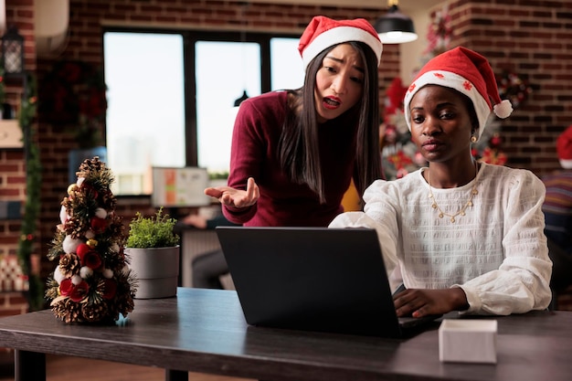 Geschäftskollegen, die im festlichen Büro Teamarbeit leisten, Brainstorming-Ideen für die Arbeit am Startup-Bericht. Arbeiten am Laptop am Arbeitsplatz mit Christbaumschmuck und Ornamenten.