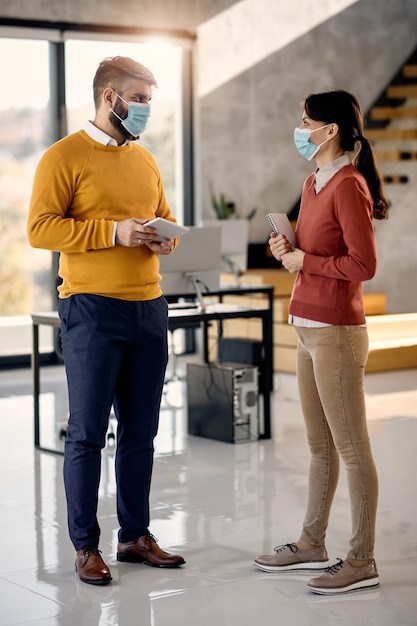 Geschäftskollegen in voller Länge mit Gesichtsmasken, die im Büro kommunizieren