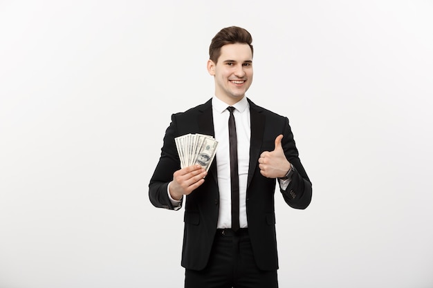Geschäftskonzept - Erfolgreicher Geschäftsmann, der Dollarnoten hält und Daumen oben lokalisiert über weißem Hintergrund zeigt.