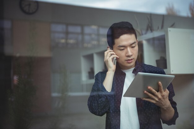 Geschäftsleiter, der auf Mobiltelefon spricht, während er digitales Tablet verwendet