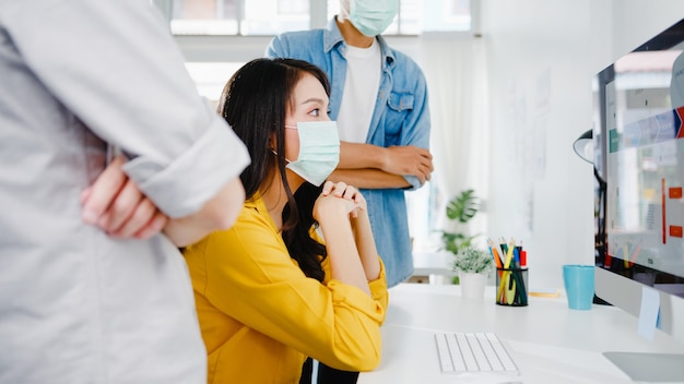 Geschäftsleute aus Asien, die Computerpräsentationen verwenden, treffen sich mit Brainstorming-Ideen über neue Projektkollegen und tragen eine schützende Gesichtsmaske in einem neuen normalen Büro. Lebensstil und Arbeit nach Coronavirus.