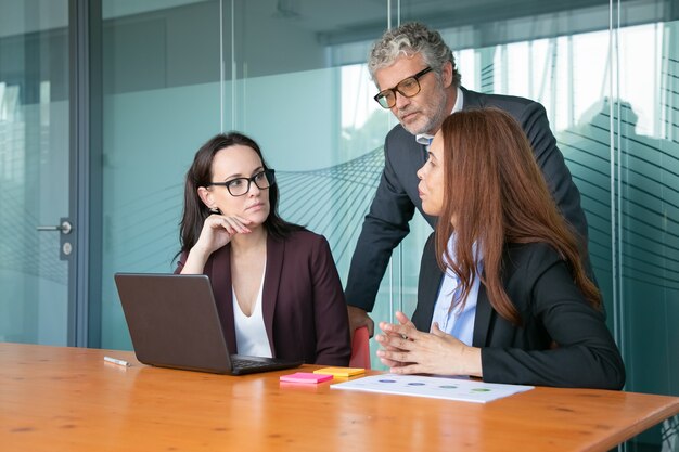 Geschäftsleute beobachten und diskutieren Präsentation auf dem PC, während sie zusammen am Besprechungstisch sitzen und stehen