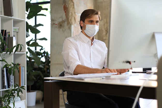Geschäftsmann arbeitet in präventiver medizinischer maske im büro.