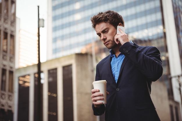 Geschäftsmann, der auf Handy spricht und Kaffee hält