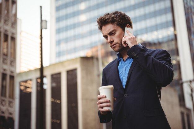 Geschäftsmann, der auf Handy spricht und Kaffee hält