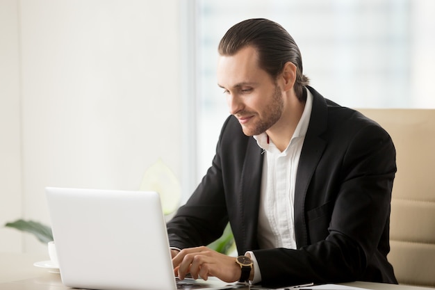 Geschäftsmann, der auf Laptop am Schreibtisch im Büro schreibt