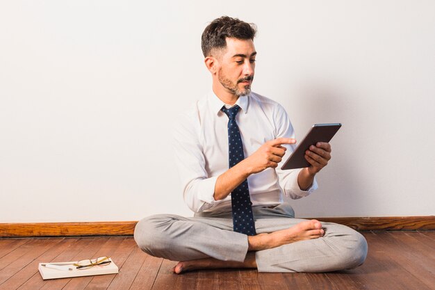 Geschäftsmann, der auf Massivholzboden unter Verwendung der digitalen Tablette sitzt