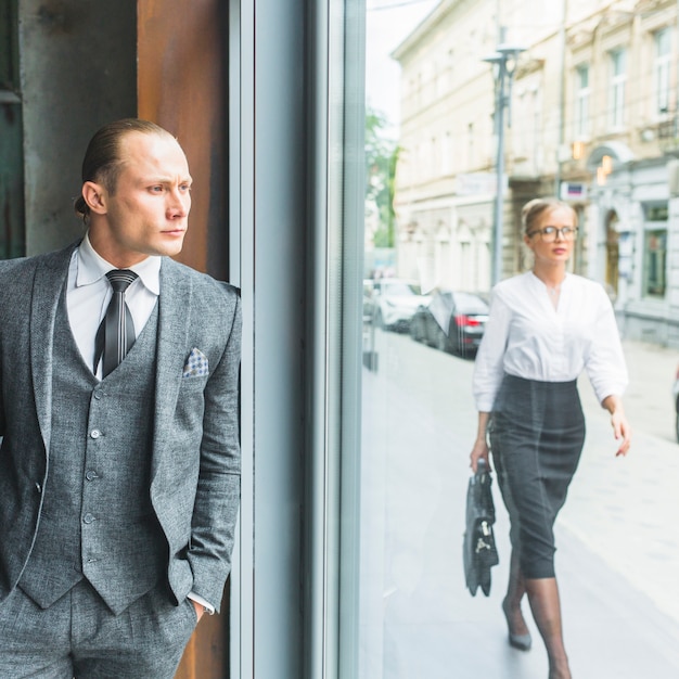 Geschäftsmann, der durch Fenster während Frau geht auf Bürgersteig schaut