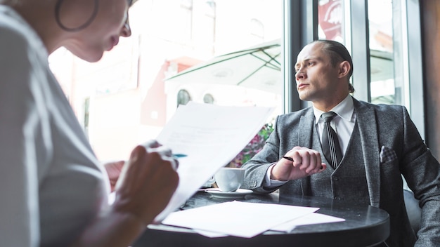 Geschäftsmann, der durch Fenster während sein Partner arbeitet an Dokument in caf? Sucht