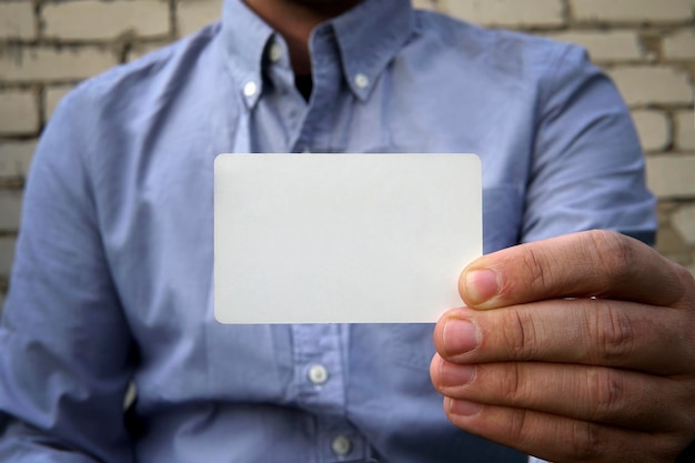 Geschäftsmann, der eine leere visitenkarte über der weißen backsteinmauer des hintergrundes auf der straße übergibt. eine plastikkreditkarte oder visitenkarte als modell für design oder text mit einem leeren raum.