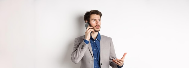 Kostenloses Foto geschäftsmann, der einen anruf tätigt, der auf dem smartphone spricht und beschäftigt aussieht, trägt einen weißen hintergrund