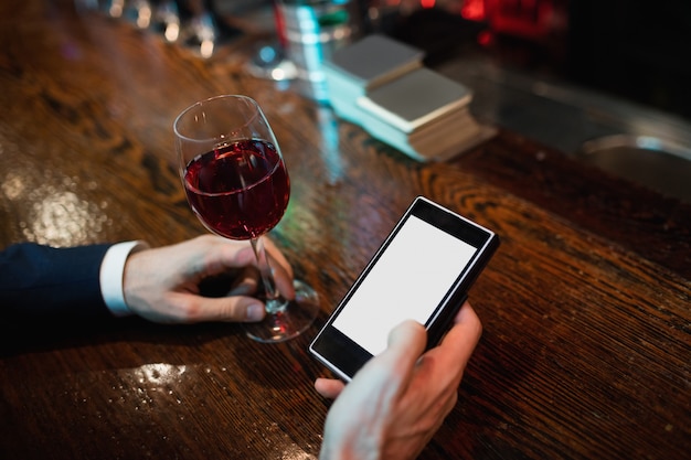 Geschäftsmann, der Handy mit Glas Rotwein in der Hand benutzt