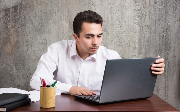 Geschäftsmann, der in Laptop schaut und am Schreibtisch sitzt. Hochwertiges Foto