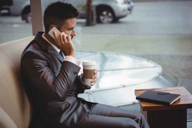 Geschäftsmann, der Kaffee hält, während auf Handy spricht