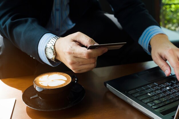 Geschäftsmann, der Kreditkarte verwendet, um online Einzelteile in der Kaffeestube zu kaufen