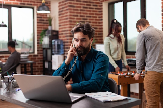 Geschäftsmann, der mit dem Manager telefoniert und den Unternehmensumsatz bespricht, während er an der Marketingstrategie im Startup-Büro arbeitet. Verschiedene Geschäftsleute, die Brainstorming-Ideen zur Planung der geschäftlichen Zusammenarbeit entwickeln