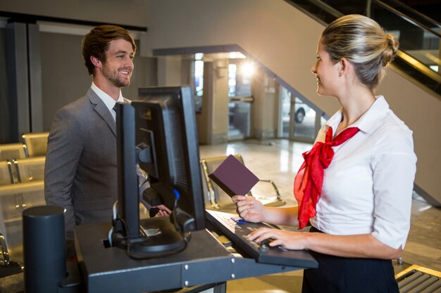 Geschäftsmann, der mit weiblichem Flughafenpersonal am Check-in-Schalter interagiert