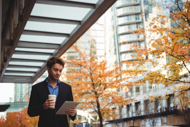 Geschäftsmann, der wegwerfbare Kaffeetasse hält und digitales Tablett verwendet