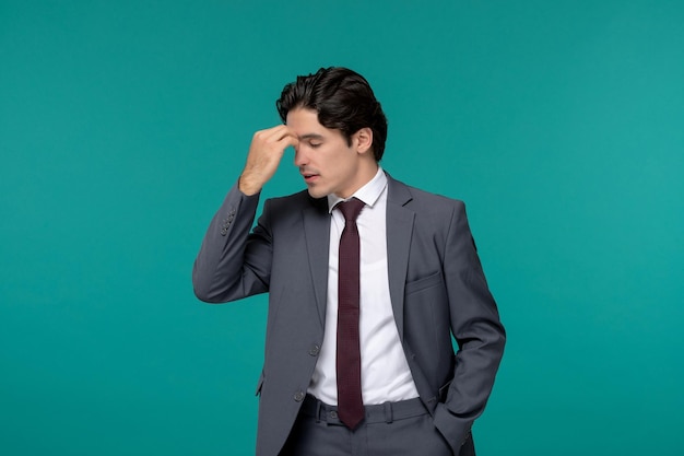 Geschäftsmann, hübscher junger brünetter Typ im grauen Büroanzug und Krawatte, die müde die Stirn hält