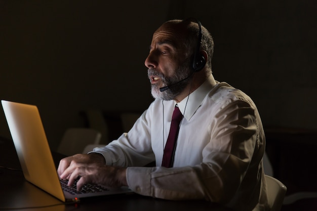 Geschäftsmann im Kopfhörer sprechend und Laptop verwendend