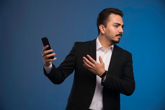 Geschäftsmann im schwarzen Anzug überprüft sein Telefon.