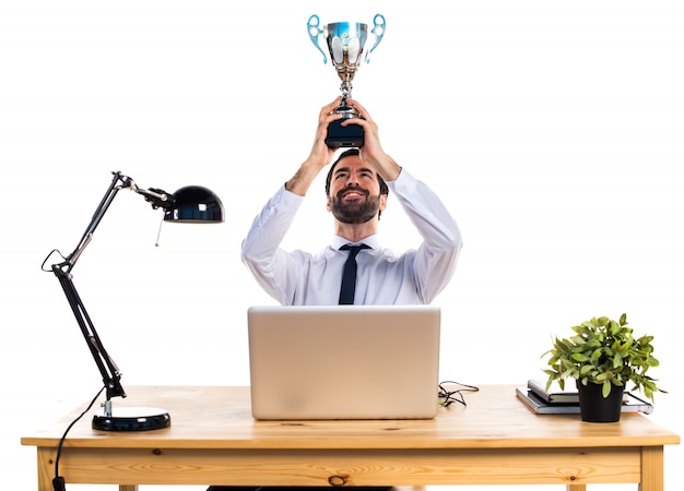 Geschäftsmann in seinem Büro hält eine Trophäe