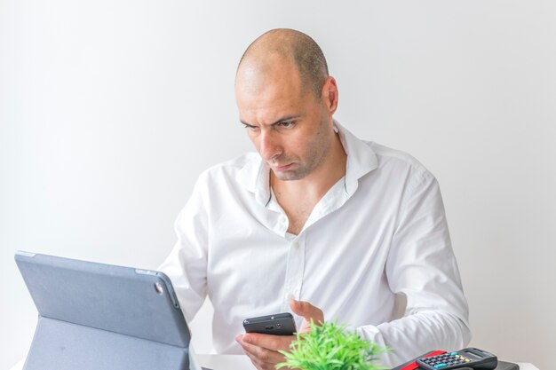 Geschäftsmann mit dem Handy, der an Laptop im Büro arbeitet