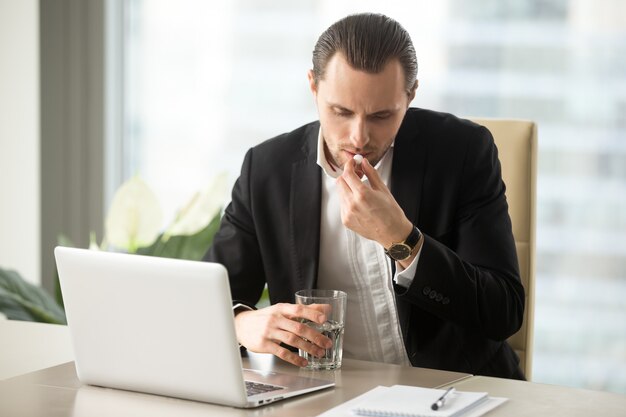 Geschäftsmann mit Glas Wasser nimmt runde Pille