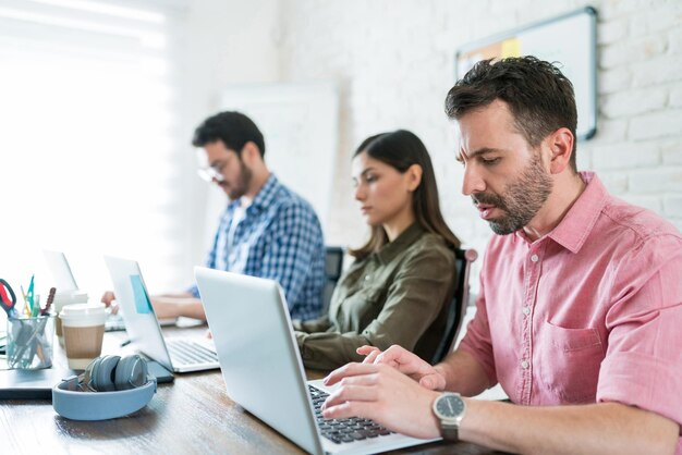 Geschäftsmann mit Laptop, während er mit jungen Kollegen am Konferenztisch im Coworking-Büro sitzt