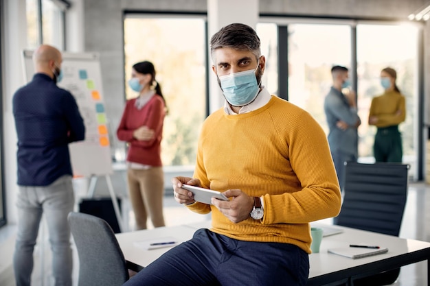 Geschäftsmann mittleren Alters, der am Touchpad arbeitet und im Büro eine schützende Gesichtsmaske trägt