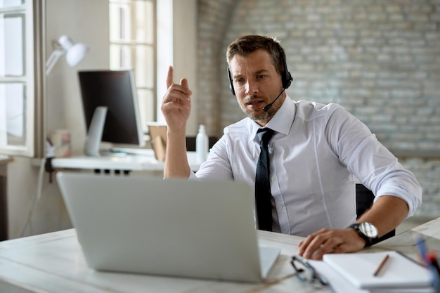 Geschäftsmann mittleren Alters mit Kopfhörern während eines Videoanrufs über Laptop im Büro