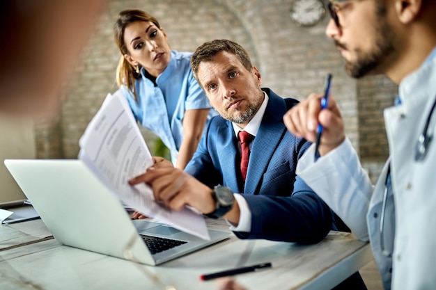 Geschäftsmann mittleren Alters und Gruppe von Ärzten, die Papierkram analysieren, während sie sich im Büro treffen