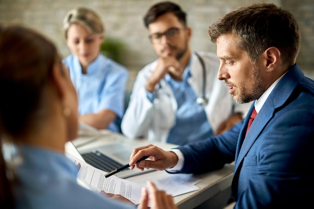 Geschäftsmann mittleren Alters und Mitarbeiter des Gesundheitswesens analysieren Dokumente während eines Meetings im Büro