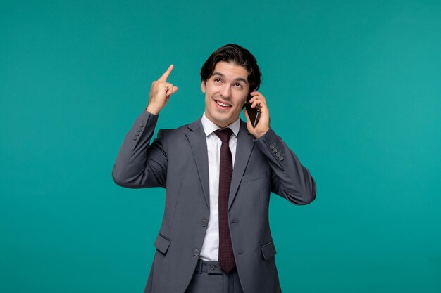 Geschäftsmann netter junger gutaussehender Mann im grauen Büroanzug und Krawatte, die am Telefon nach oben zeigt