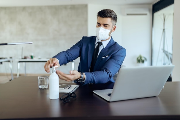 Geschäftsmann trägt Gesichtsmaske und verwendet Händedesinfektionsmittel, während er im Büro arbeitet