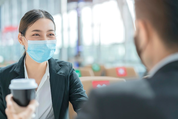 Geschäftsmann und Frau mit Gesichtsmaskenschutz beiläufiges Treffen am Sitzplatz mit sozialer Distanzierung am neuen Lifestyle-Geschäftskonzept des Flughafenterminals