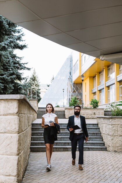 Geschäftsmann und Geschäftsfrau, die das Mobiltelefon und digitale Tablette außerhalb des Büros zusammen gehen hält