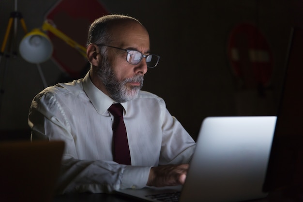 Geschäftsmann unter Verwendung des Laptops im dunklen Büro