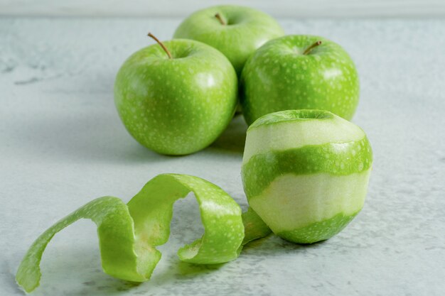 Geschälte und ganze frische grüne Bio-Äpfel auf grauer Oberfläche