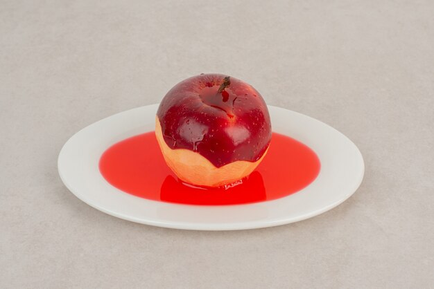 Geschälter roter Apfel auf Saft auf weißem Teller.