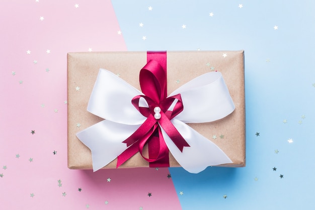 Geschenk oder präsentkarton mit einem großen bogen auf einer rosa blauen tischplatteansicht. flache laienzusammensetzung für weihnachten, geburtstag, muttertag oder hochzeit.