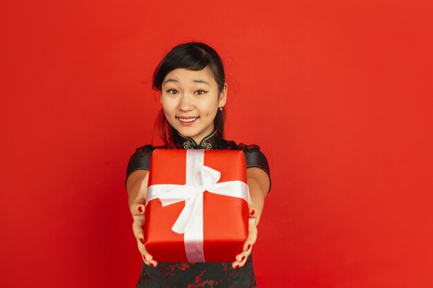 Geschenkbox geben. Frohes chinesisches neues Jahr 2020. Porträt des asiatischen jungen Mädchens lokalisiert auf rotem Hintergrund. Weibliches Modell in traditioneller Kleidung sieht glücklich aus. Feier, Urlaub, Emotionen. Copyspace.