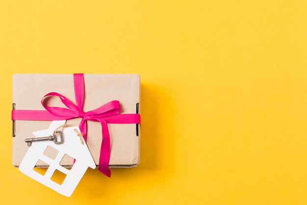 Geschenkbox gebunden mit Schlüssel und Hausmodell über hellem gelbem Hintergrund