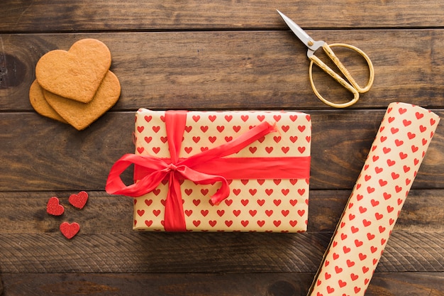 Geschenkbox in der Nähe der Rolle Süßpapier, Schere und Kekse