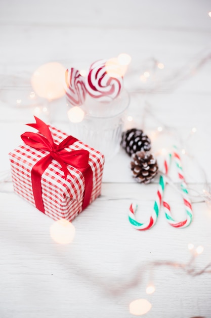 Geschenkbox in der Nähe von Glas mit Lutschern, Zuckerstangen und beleuchteten Lichterketten